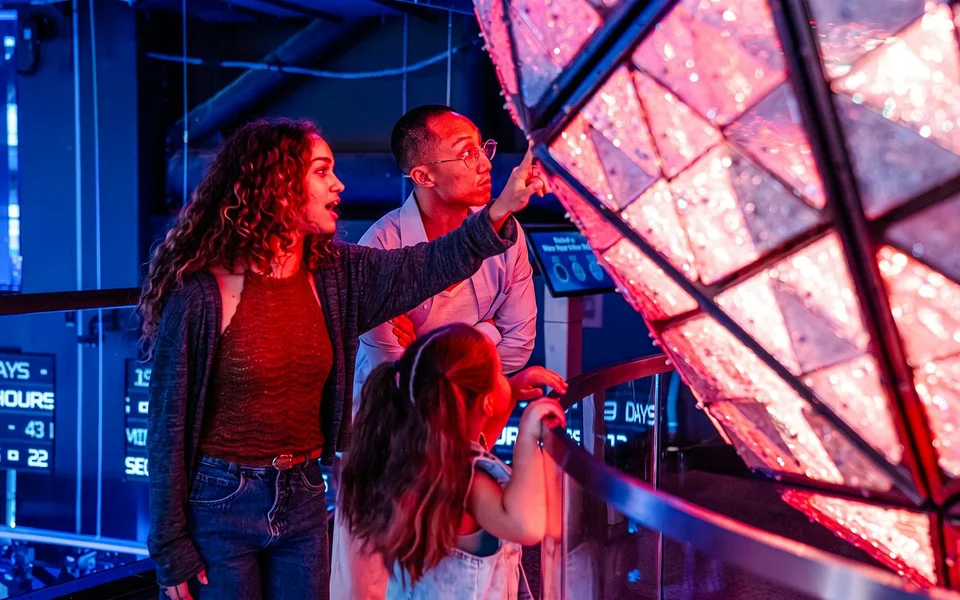 Visitatori osservano una sfera luminosa di Capodanno in mostra